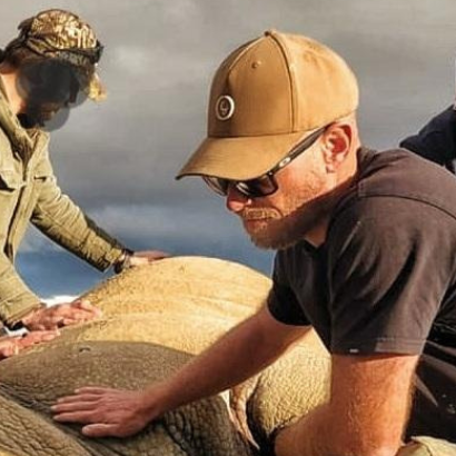 Three men working on a large animal, likely a rhinoceros, in an outdoor setting.